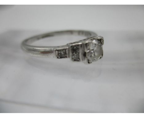 A white metal ring with a diamond in a square setting, flanked by stepped shoulders, each with three diamonds, stamped platin