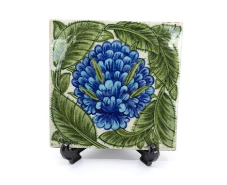 William De Morgan for Merton Abbey Pottery tile with blue flower and green leaves. Approx 15cm square. Impressed marks to the