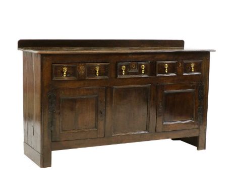 An oak dresser base, 18th century, three drawers with moulded fronts and cupboards, brass drop handles, iron bracket hinges, 
