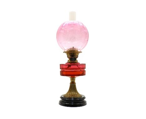 A Victorian cranberry glass oil lamp, with a faceted well, raised on an embossed spreading brass column and black glass base,