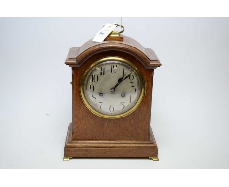 A Victorian oak mantel clock, the silvered dial with arabic numerals in black, on brass bracket feet, 33cms high.