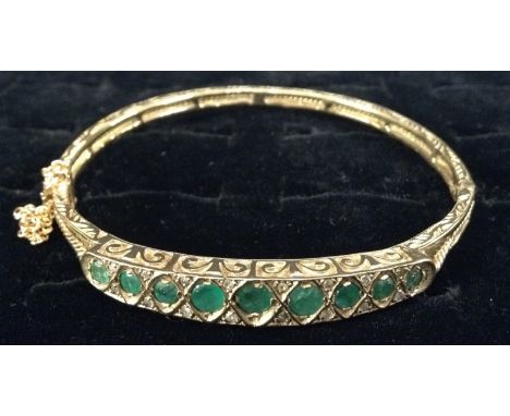 An Edwardian emerald and diamond hinge bangle, central row of nine graduated emeralds, each divided by a pair of round cut di