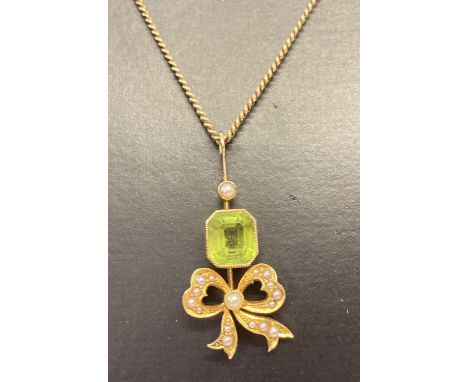 An antique 18ct gold peridot and seed pearl pendant with bow detail on a 14ct gold fine curb chain.  Drop pendant set with an