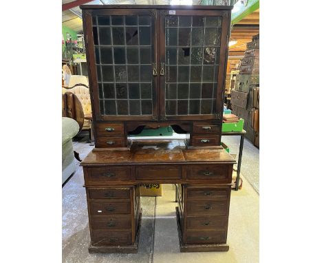 Edwardian oak kneehole writing cabinet, two lead coloured glass doors above hinged writing service with six pedestal drawers,