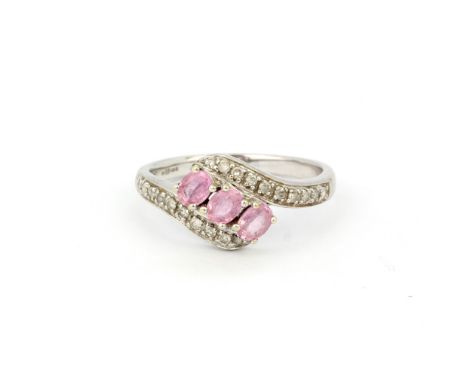 A hallmarked 9ct white gold crossover ring set with oval cut pink sapphires and diamonds, (P.5).