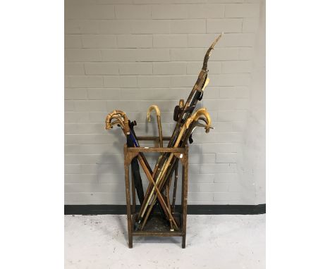 An oak stick stand with tray, together with a large quantity of assorted walking sticks and umbrellas including many examples