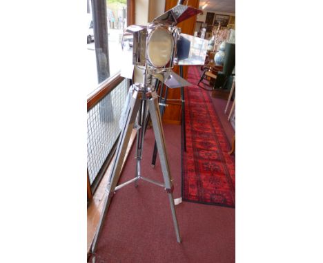 A chromed studio light with barn door shades and raised on wooden tripod supports