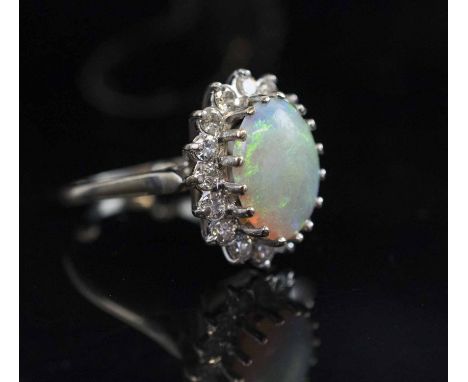 AN OPAL AND DIAMOND CLUSTER RING, the oval shaped opal mounted in 18 carat white gold within a surround of sixteen brilliant 