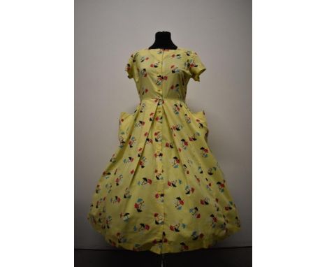 A 1950s yellow cotton day dress having novelty parasol print in pink, black, blue and white with large pockets and buttons to