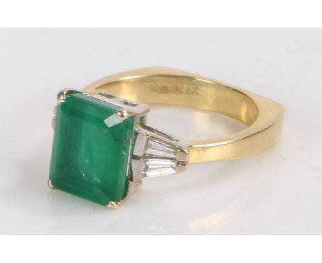 18 carat gold emerald and diamond set ring, the central emerald at approximately flanked by two diamonds to either side, ring