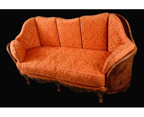 A Louis XV Revival mahogany bombe shaped bergère sofa, carved throughout with lotus paterae, bell husks, scrolling acanthus, 