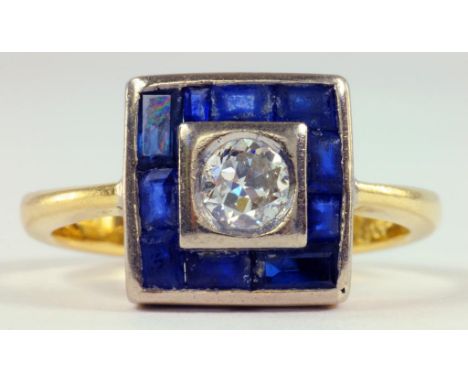 A SAPPHIRE AND DIAMOND CLUSTER RING, THE ROUND BRILLIANT CUT DIAMOND IN A SQUARE SURROUND OF CALIBRE CUT SAPPHIRES IN GOLD, M