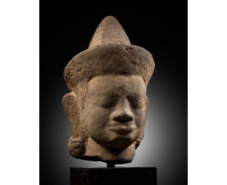 A MONUMENTAL SANDSTONE HEAD OF A MALE DEITY, ANGKOR WAT STYLEKhmer Empire, 12th century. The face with a serene expression ma