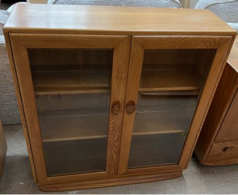 An Ercol light elm bookcase with a pair of bevelled glass doors on a plinth base, 91.5cm wide x 98cm high 