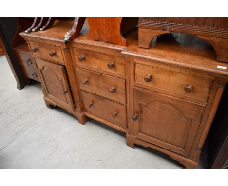 A traditional solid oak sideboard having recessed three drawer centre section flanked by drawers and cupboard, turned handles
