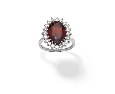 GARNET AND DIAMOND CLUSTER RING, 1989The oval-cut garnet within a surround of brilliant-cut diamonds, mounted in 18 carat whi