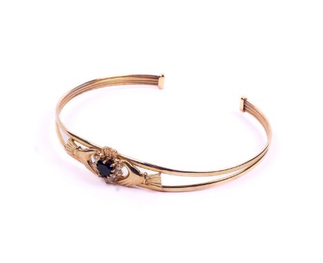 A 9ct yellow gold Claddagh style bangle. Set centrally with a faceted heart shaped sapphire of approximately 0.60 carats with