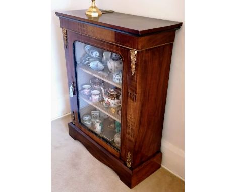 A Victorian walnut display cabinet with glazed door, shelved interior, ormolu mounts and inlaid floral decoration on a shaped