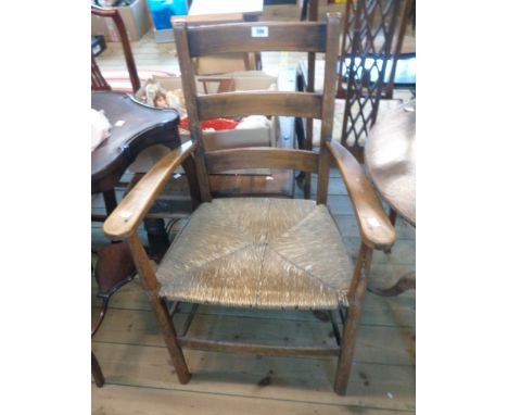 An old stained beech framed ladder back elbow chair with woven rush seat and simple turned supports