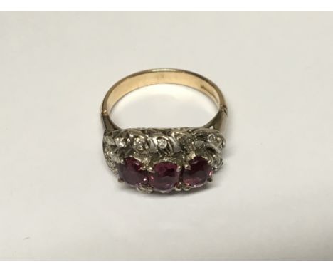 A Ruby and diamond Ladies ring set with three Ruby’s surrounded by diamonds in an open scroll work. Ring marked 18ct, Ring si