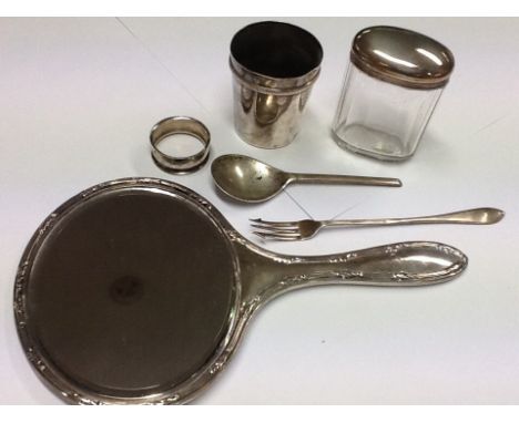 A silver backed mirror, a white metal beaker, spoon, fork, napkin ring, and tidy jar, all silver.