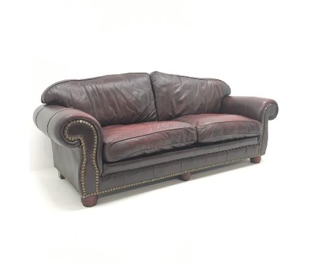 Three seat sofa upholstered in studded oxblood leather, arched back, scrolled arms, turned supports (W230cm) and matching two