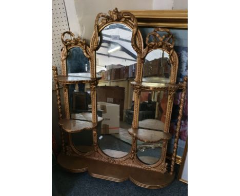 A gilt overmantle mirror 87cm x 76cm The central oval mirror flanked by smaller mirror, the side mirrors having two shelves e