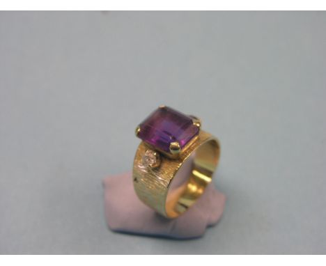 A yellow metal ring, step-cut amethyst and two clear stones, bark-effect, bearing stamp 18ct.