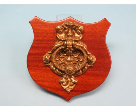 A large Baroque-style brass door-knocker, cast with cherubs and masks, mounted upon mahogany shield, shield 12in. wide