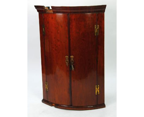 GEORGIAN FIGURED MAHOGANY BOW FRONTED CORNER CUPBOARD, the moulded cornice above a pair of cupboard doors with exposed brass 