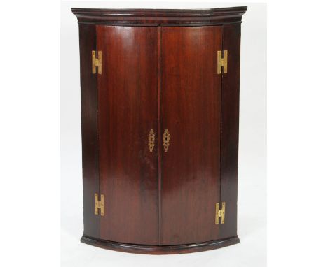 GEORGE III DARK MAHOGANY BOW FRONTED CORNER CUPBOARD, the moulded cornice above a pair of cupboard doors, fitted with exposed