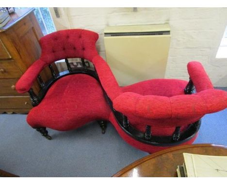 A late Victorian ebonized and red upholstered conversation seat, in a floral design, on turned legs and brass/ceramic castors