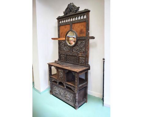 A tall late 19th Century carved oak hall stand with carved face pediment, tapestry panelled and carved back with round centra