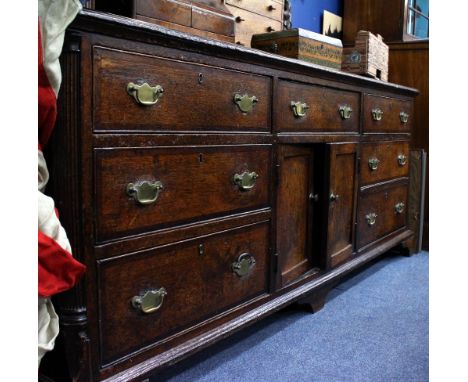 A GEORGE III OAK DRESSER BASE with seven drawers around central cupboard doors with reeded canted corners and standing on bra
