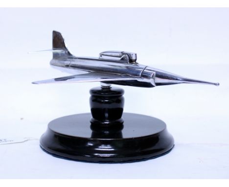 A CHROME PLATED TABLE LIGHTER  in the form of a model swept wing aircraft, mounted on an ebonised base 16cm wide  provenance 
