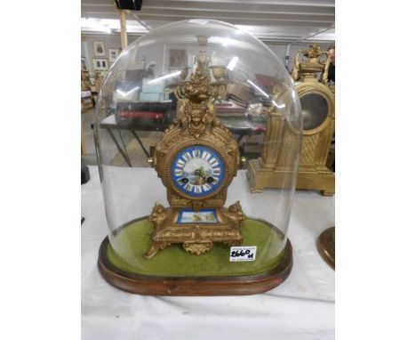 A gilt clock with enamel dial under glass dome.