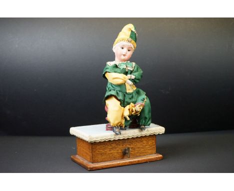 Early 20th century Musical Automaton in the form of a Bisque Head Doll dressed in a green and yellow clown outfit sat in a wo