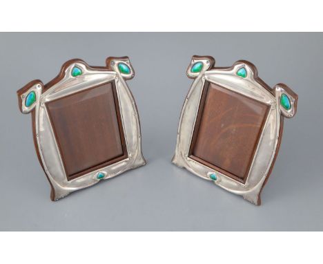 A matched pair of Edwardian Art Nouveau silver and enamel photograph frames, with stylised decoration and four enamelled pane