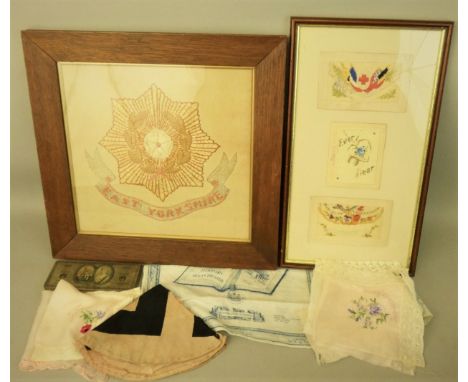 A framed East Yorkshire Regiment embroidered badge 40 x 41cm, three framed WWI souvenir embroidered postcards 43 x 23cm, a 19