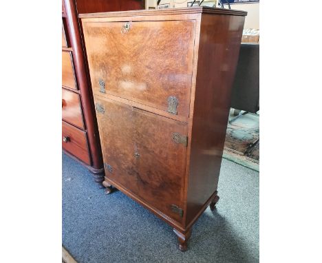 A burr walnut drinks cabinet, the fall front revealing a mirrored and glazed interior, the doors beneath revealing a 3/4 shel