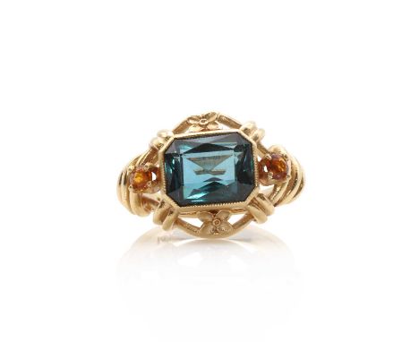 A gold and synthetic blue spinel ring, a scissor cut synthetic blue spinel bezel set to an open gallery, flanked by a circula