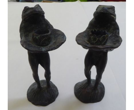 A pair of patinated green bronze novelty candle holders, each featuring a frog holding a lily pad&nbsp; 9"h&nbsp; 