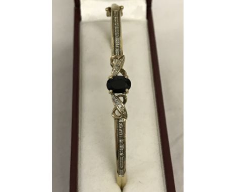 9ct gold hinged bangle set with oval sapphire and 10 small diamonds. Decorative mount with crossover design to each side of t