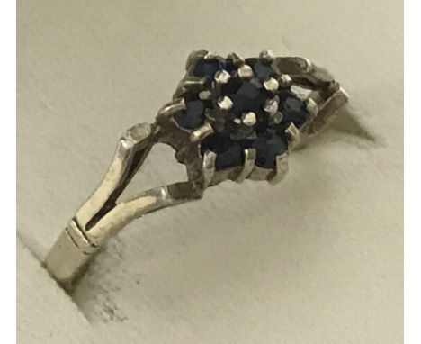 A 9ct gold sapphire cluster style dress ring. Small central round cut sapphire surrounded by 6 other small sapphires. Unusual