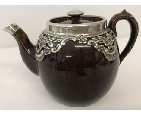 A ceramic teapot brown glaze teapot with silver clad rim and silver floral decoration to body. Finial to lid and spout also c