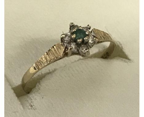 A 9ct gold small flower design emerald and diamond dress ring. Small central round cut emerald surrounded by 6 small diamonds