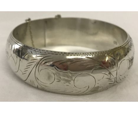 Silver hinged bangle with decorative engraving. Approx. 2cm deep. Slight dent to one side and safety chain broken. 