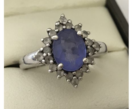 A ladies silver stone set dress ring. Central oval blue stone surrounded by 20 smaller clear stones. Size O 1/2.