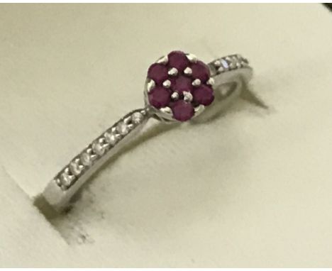 A 9ct white gold ruby and diamond dress ring. Central small ruby surrounded by 6 other rubies.  7 small diamonds set to each 