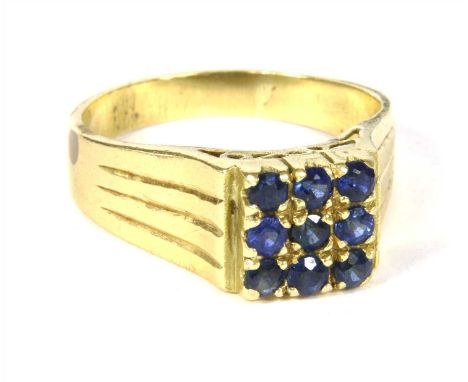 A gold sapphire ring, the square head grain set with round cut sapphires, to grooved flat section tapered shoulders and a pla